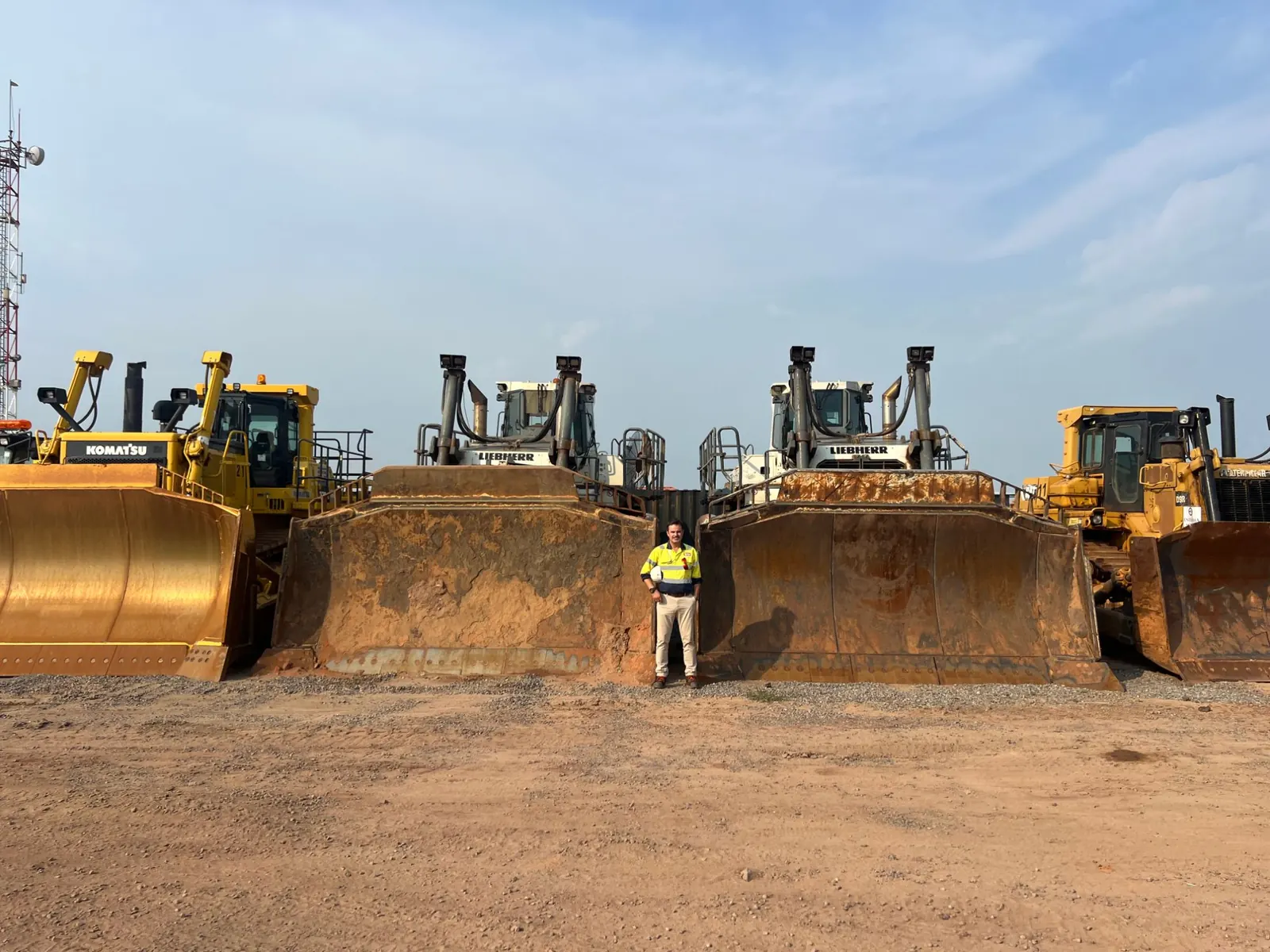 TMS field engineer standing between the blades of a fleet of mining dozers